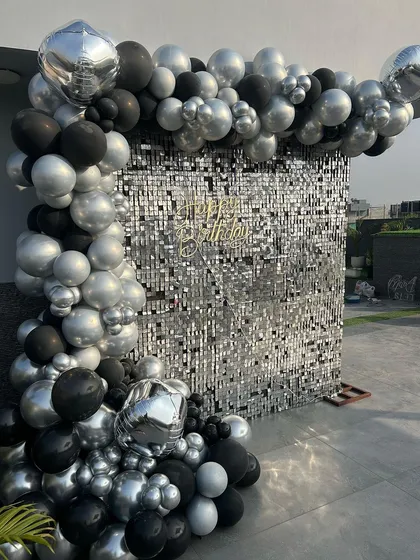 A chic and modern birthday backdrop with a silver shimmer wall framed by a black and silver organic balloon garland. This sleek design is perfect for sophisticated corporate parties and rooftop events.
