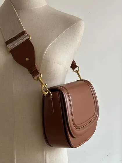 Another view of the Noble bag on a mannequin, showing its profile when worn. The high-quality brass hardware really stands out against the brown leather.