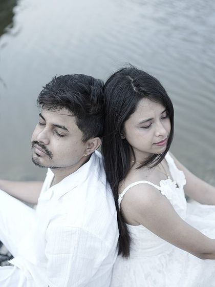 A peaceful moment of a couple sitting back-to-back by the water, eyes closed, creating a serene and connected portrait.
