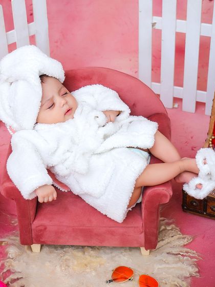 A close-up of the baby relaxing in the spa-themed setup, showing off the adorable details of the tiny bathrobe and the peaceful sleeping expression.