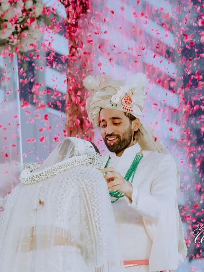 A beautiful moment during the varmala ceremony, as the groom lovingly places the garland, framed by a modern floral mandap and a shower of pink petals.