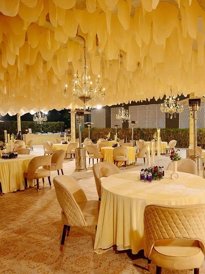 A wide view of the reception seating area, featuring a cloud-like ceiling of white fabric, sparkling chandeliers, and elegant guest tables.