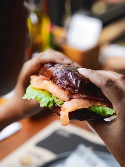 A customer holding one of our lye-dipped bagel sandwiches, filled with fresh ingredients.
