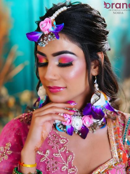 A vibrant Haldi and Mehendi look, featuring colorful floral jewelry and bright, playful eye makeup with a sunset blend of pink, yellow, and orange.