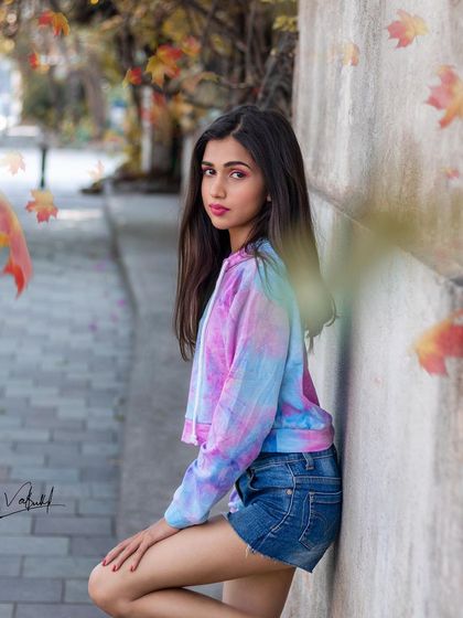 A subtle and stylish street portrait with a touch of autumn feeling from the falling leaves effect. The model's casual pose and tie-dye hoodie create a simple, relatable, and fashionable image.