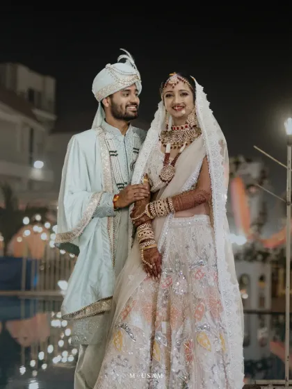 A couple in a dreamy pastel color palette. The bride's white and pastel lehenga and the groom's powder blue sherwani create a soft, modern, and elegant look, perfect for a daytime or evening wedding.