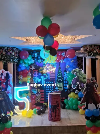 We brought the Avengers to this 5th birthday party with a full superhero theme. The decoration includes a city skyline backdrop, character cutouts of Spiderman, Batman, Hulk, and Thor, a large light-up number '5', and colorful balloon arrangements.