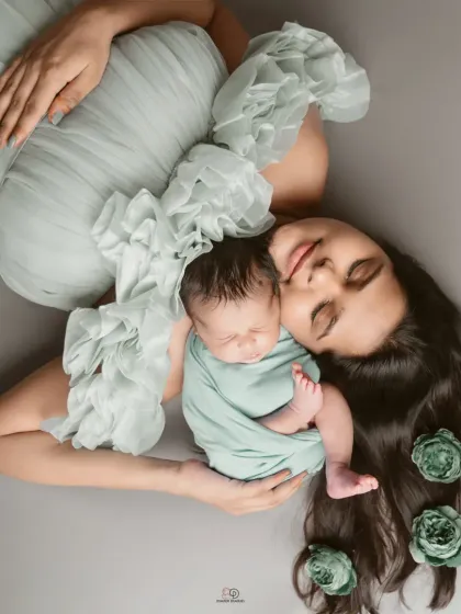 An artistic overhead portrait of a mother and her newborn. The baby is nestled beside his mother, whose hair is decorated with matching flowers, creating a beautiful, fine-art look.