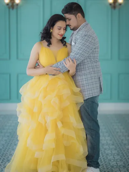 An intimate studio portrait of an expecting couple. Her bright yellow gown brings a cheerful warmth to the image, while their close embrace against a simple teal backdrop captures a quiet moment of connection and anticipation.