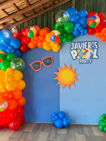 A bright and sunny pool party theme, with a colorful balloon arch, beach ball balloons, and fun sun and sunglasses cutouts.