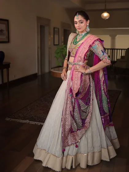 A full-length view of this majestic outfit, showcasing the contrast between the ivory skirt and the colorful, heavily embroidered blouse and dupattas.