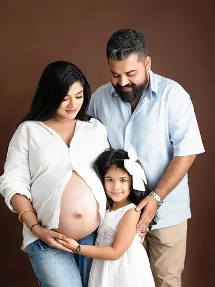 A complete family portrait during a studio maternity shoot. This image captures the family unit before the new baby arrives, set against a warm, neutral backdrop.