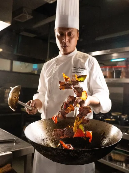 An action shot of a chef tossing beef and peppers in a wok. This behind-the-scenes photo shows the skill and energy of the kitchen.