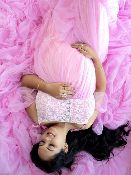 An artistic overhead shot of a mom-to-be lying in a sea of pink fabric from her gown, creating a beautiful and unique composition.