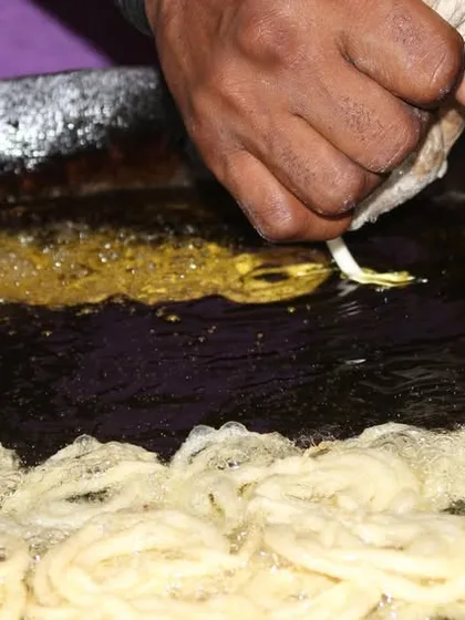 A close-up of our chef skillfully piping jalebi batter into hot oil. This is how we create those perfect, syrupy swirls that are a staple of any celebration.