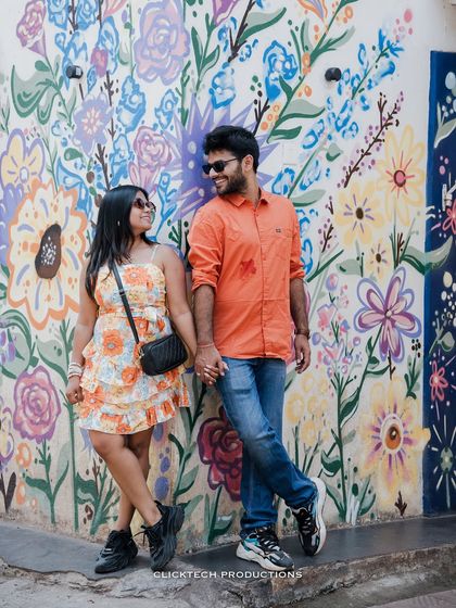 A stylish, full-length shot of a couple posing against a colorful floral mural in Goa, perfect for a modern and artistic pre-wedding shoot.