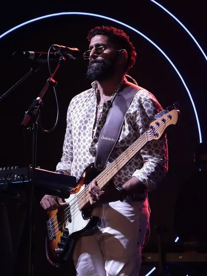A member of Sanam Band on the bass guitar, performing against a backdrop of custom neon rings, fully integrating the entertainment with the event's theme.