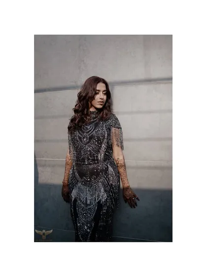 A striking portrait of the bride-to-be in a glamorous, fringed dress. The play of light and shadow highlights the intricate details of her outfit and her confident presence.