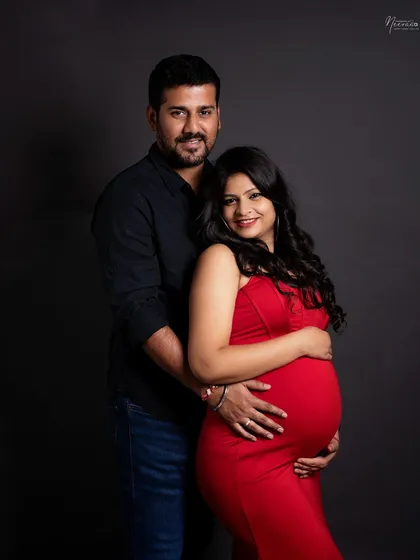A classic and elegant couple's portrait. The way they hold each other and the baby bump shows their strong connection and shared joy. The simple dark background keeps the focus entirely on them.