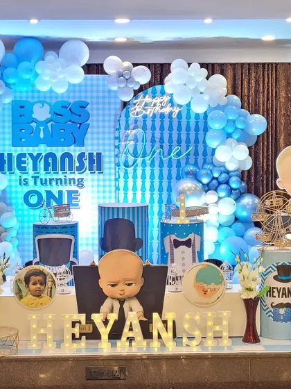 A fun and stylish Boss Baby themed birthday stage. The setup includes a custom light-up backdrop, character cutouts, themed pedestals for the cake, and marquee letters spelling out the birthday boy's name.