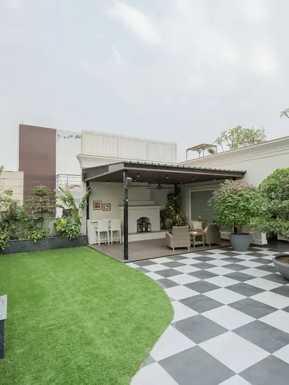 This is what a modern, functional, and beautiful terrace looks like. We combined bold checkered flooring with soft, natural grass and a variety of tropical plants to create a space that feels both expansive and intimate, complete with a covered seating area and a custom bonsai feature.