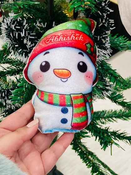 A close-up of our adorable snowman plush ornament, hanging on a Christmas tree.