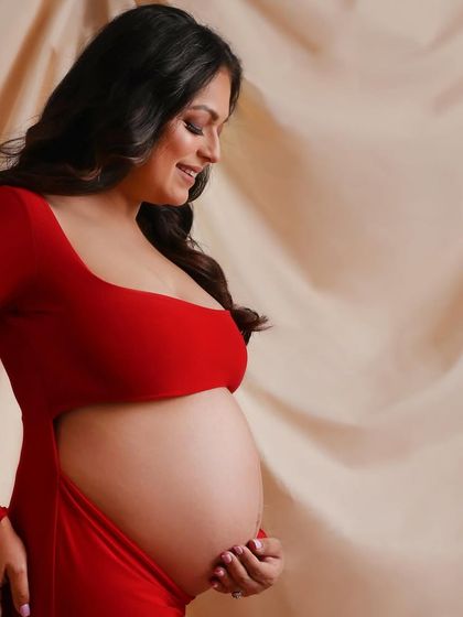 A close-up detail shot, focusing on the beautiful curve of the baby bump in this vibrant red dress.