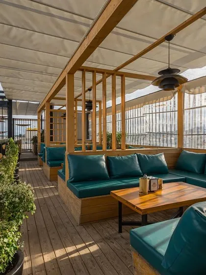 This view shows the spacious layout of the rooftop seating area. The combination of natural wood, comfortable upholstery, and open air creates a relaxed and upscale lounge environment.