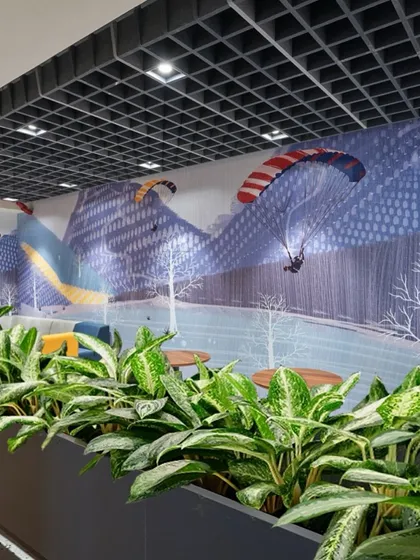 A row of lush green plants in a large planter, set against a wall with a mountain-themed mural. This combination of real and illustrated nature adds depth and interest.