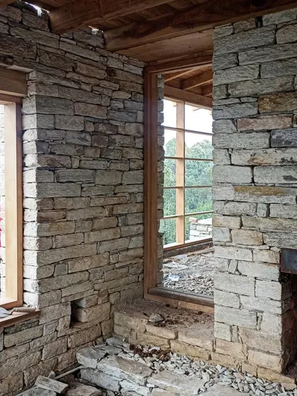 A detail of the hand-stacked stone walls inside a Himalayan project. The variations in color and texture of the local stone are a key feature of the design, connecting the interior directly to the geology of the site.