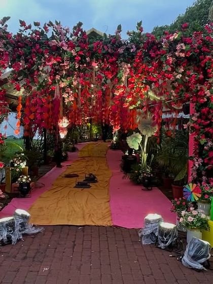 An immersive wedding entrance created with a dense canopy of red and pink bougainvillea. This design makes guests feel like they are walking through a secret garden.