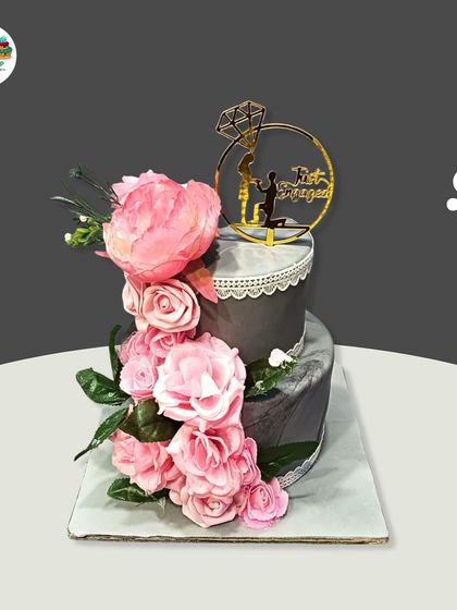 This two-tiered engagement cake features a cascade of handmade pink sugar peonies against a sophisticated grey marble fondant. A custom topper with a proposal silhouette adds a romantic finishing touch.