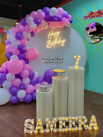 A full view of Sameera's 7th birthday party setup. The purple and pink balloon arch is paired with a white backdrop and light-up props.