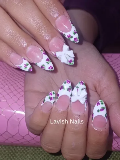 A delicate and feminine design on long, almond-shaped nails. This set combines a French manicure base with intricate, hand-painted purple floral patterns and is finished with a beautifully sculpted 3D white bow for an elegant, textured look.