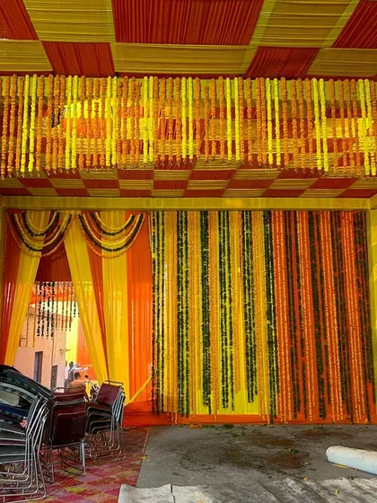 A full view of a pandal we set up for a home wedding. The ceiling features a checkered pattern of yellow and orange fabric, with dense marigold hangings creating a rich, traditional look.