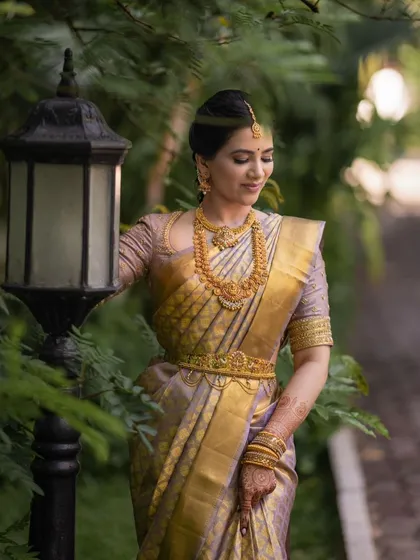A full-length professional shot capturing the elegance of this South Indian bride. The makeup is subtle yet defining, perfect for her lavender and gold saree.