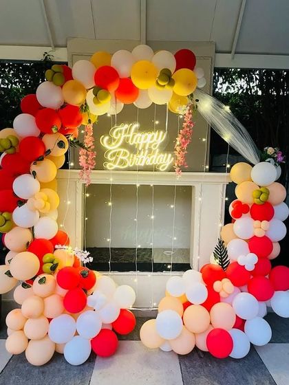 A warm and inviting birthday setup with a red, orange, and white balloon arch over a window frame.