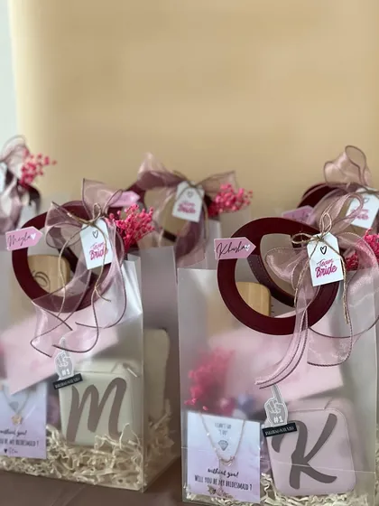 A closer look at these budget-friendly bridesmaid hampers, all wrapped up and ready to go. The translucent bags with maroon handles give a chic preview of the personalized gifts inside.