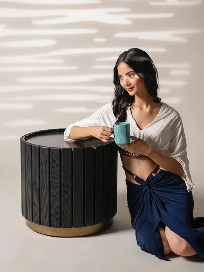 A lifestyle shot for INDY, showing a model interacting with a modern, fluted side table. This image effectively showcases both the furniture and the fashion in a relaxed, candid moment.