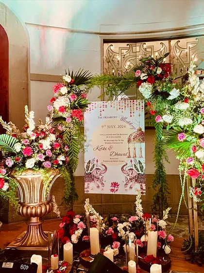 A beautiful welcome setup featuring a personalized sign with elephant motifs, surrounded by candles and lush arrangements of red and white flowers.