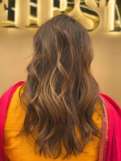 A back view of a client's hair with a beautiful, warm color and soft waves. This look is perfect for adding a touch of elegance and sophistication to your style.