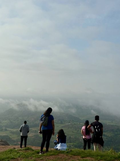 Trekkers enjoying the view from the top of Uttari Betta, looking down at a valley filled with clouds.