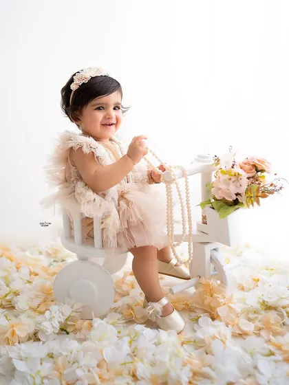 A happy baby girl on her tricycle, surrounded by a floor of white petals.