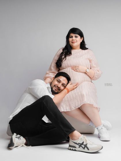A modern and stylish maternity photo against a simple grey backdrop. The couple's relaxed pose and genuine smiles show their excitement and connection as they await their little one.