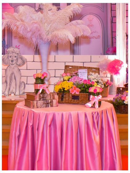 A close-up of a table centrepiece, with a tall vase of pink ostrich feathers, a basket of flowers, and a poodle cutout, all contributing to the chic Parisian vibe.