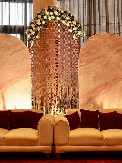 A modern stage design with a touch of tradition, featuring arched backdrops with marble and jaali patterns, softened by white floral arrangements.