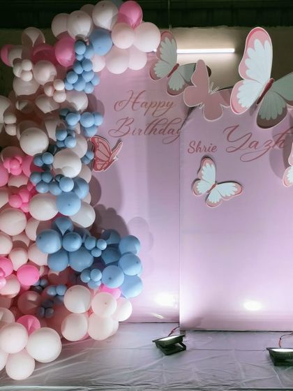 A simple yet elegant butterfly themed photo backdrop, using a soft pink panel and a cascade of pink, white, and blue balloons.