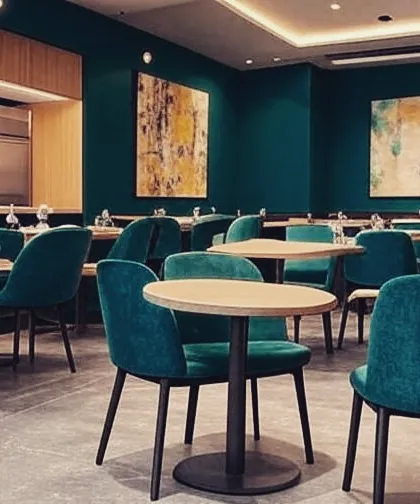 A close-up view of the dining setup in a modern restaurant, showcasing the teal velvet chairs and simple wooden tables. The design focuses on color and comfort to enhance the guest experience.