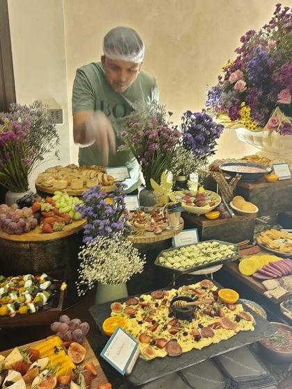 A member of my team adding the final touches to a beautiful grazing table for a birthday celebration. The table is adorned with fresh flowers and features a wide variety of appetizers and cheeses.