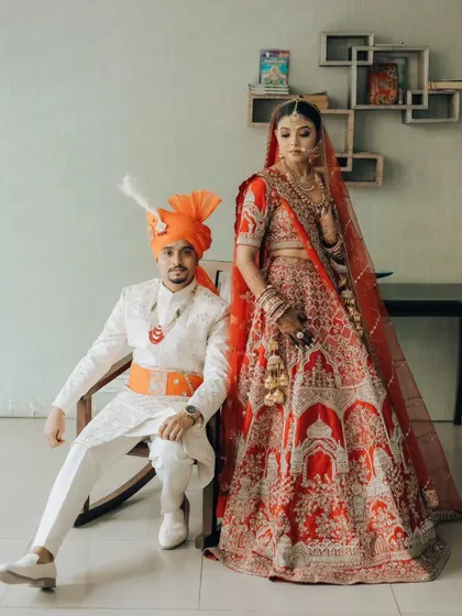 A modern royal portrait. The groom seated, the bride standing tall beside him, this pose creates a sense of partnership and regal elegance against a simple backdrop.